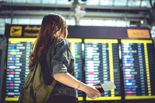 A young woman stands in front of airport departure screens