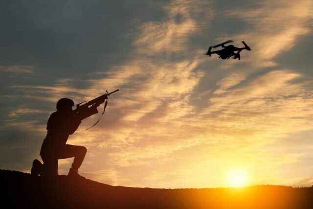 Soldier trying to shoot down reconnaissance drone against the backdrop of a sunset.