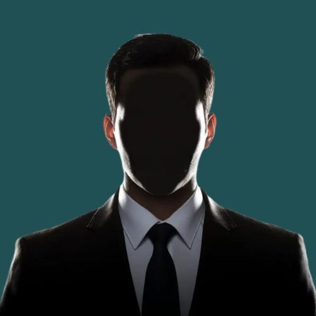 A silhouetted figure in a dark business suit and tie against a teal background, with dramatic backlighting that obscures facial features while highlighting the professional attire and formal presentation.