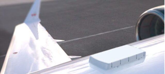 A white plastic shopping bag sits on what appears to be a car's surface, with part of the vehicle's wheel visible in the background on asphalt pavement.