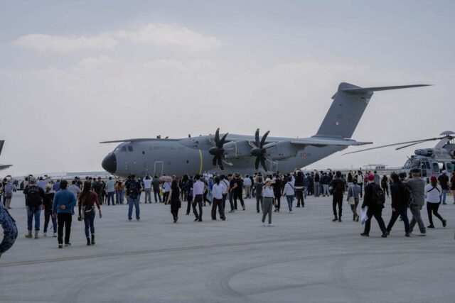 A large military transport aircraft with twin propellers is displayed on an airport tarmac, surrounded by crowds of visitors at what appears to be an air show or public aviation event.