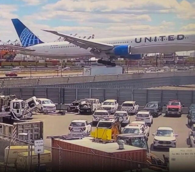 A United Airlines aircraft sits on the tarmac at an airport while numerous ground service vehicles and equipment are positioned on the ground level below, with airport infrastructure and a cloudy sky visible in the background.