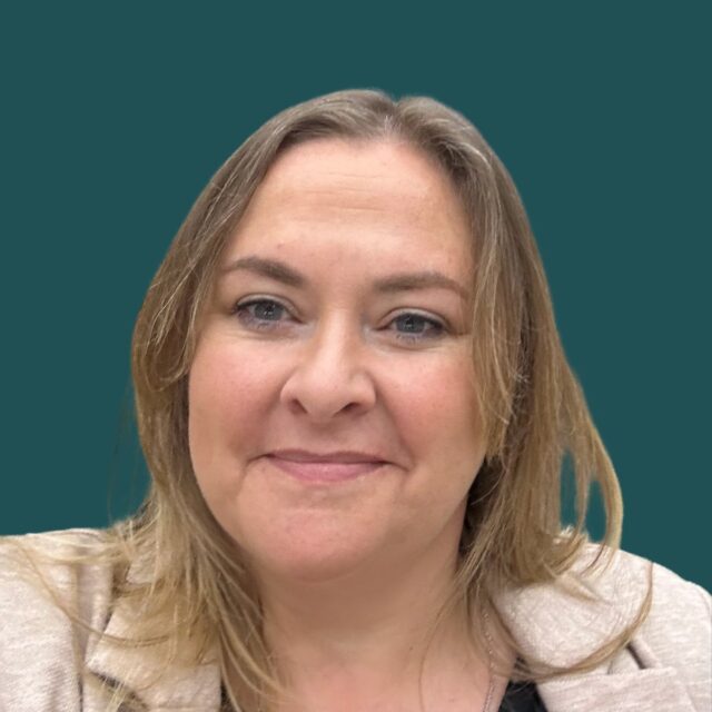 A woman with shoulder-length blonde hair and blue eyes smiles warmly at the camera, wearing a light-colored blazer against a teal background in what appears to be a professional headshot.
